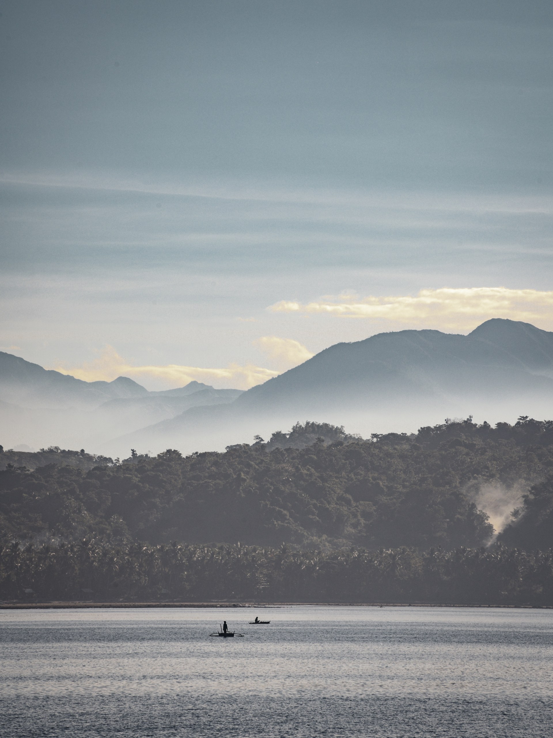 Fishermen in small outrigger boats on calm water beneath misty mountains, Sablayan, Philippines