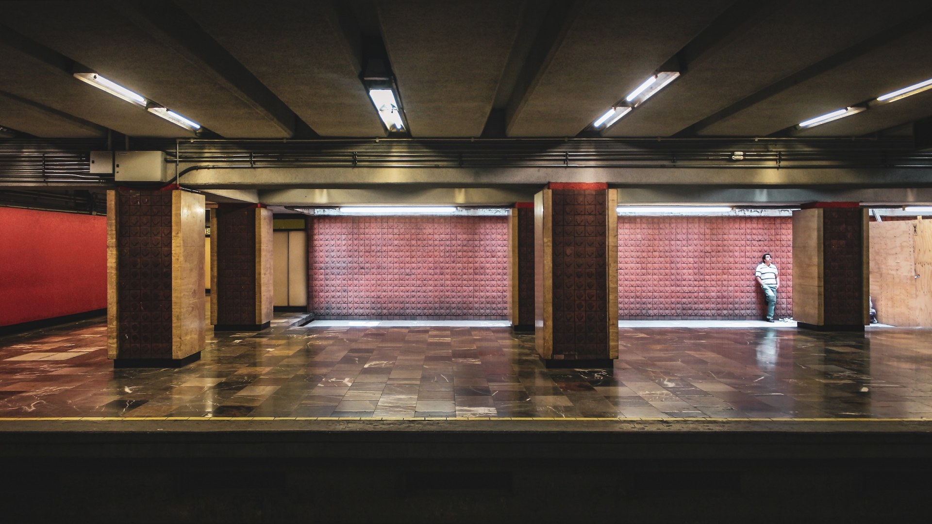 Lone man leaning against a red-tiled wall in an empty metro station, Mexico City