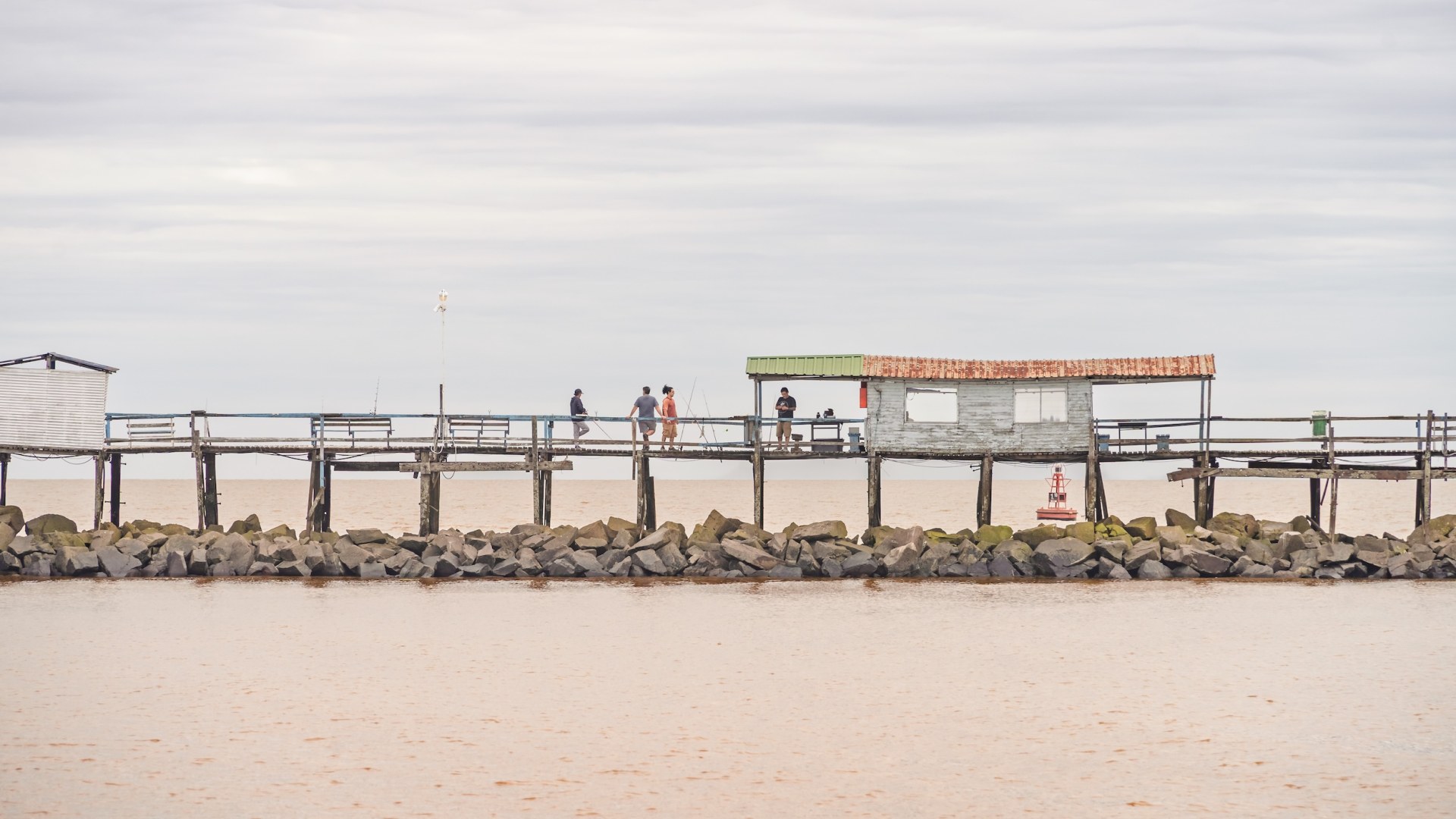 Anglers on an old wooden pier above brown water in Buenos Aires, Argentina