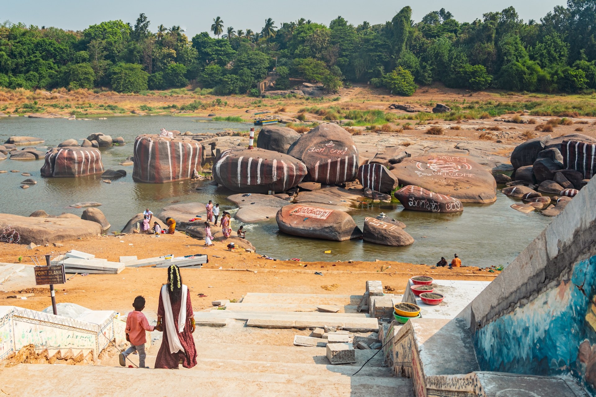 Woman and child walking down to the river between large boulders in Hampi, India
