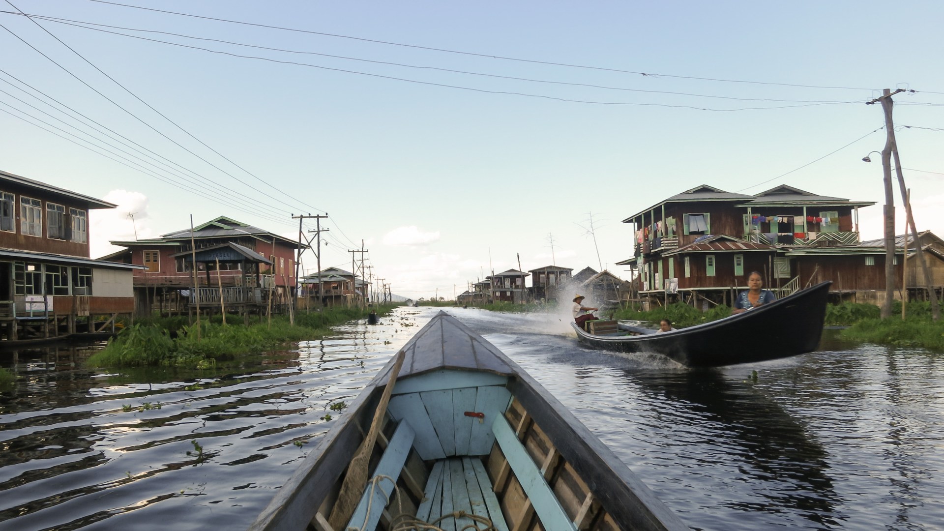 View from the bow of a wooden boat along a canal lined with stilt houses on Inle Lake, Myanmar