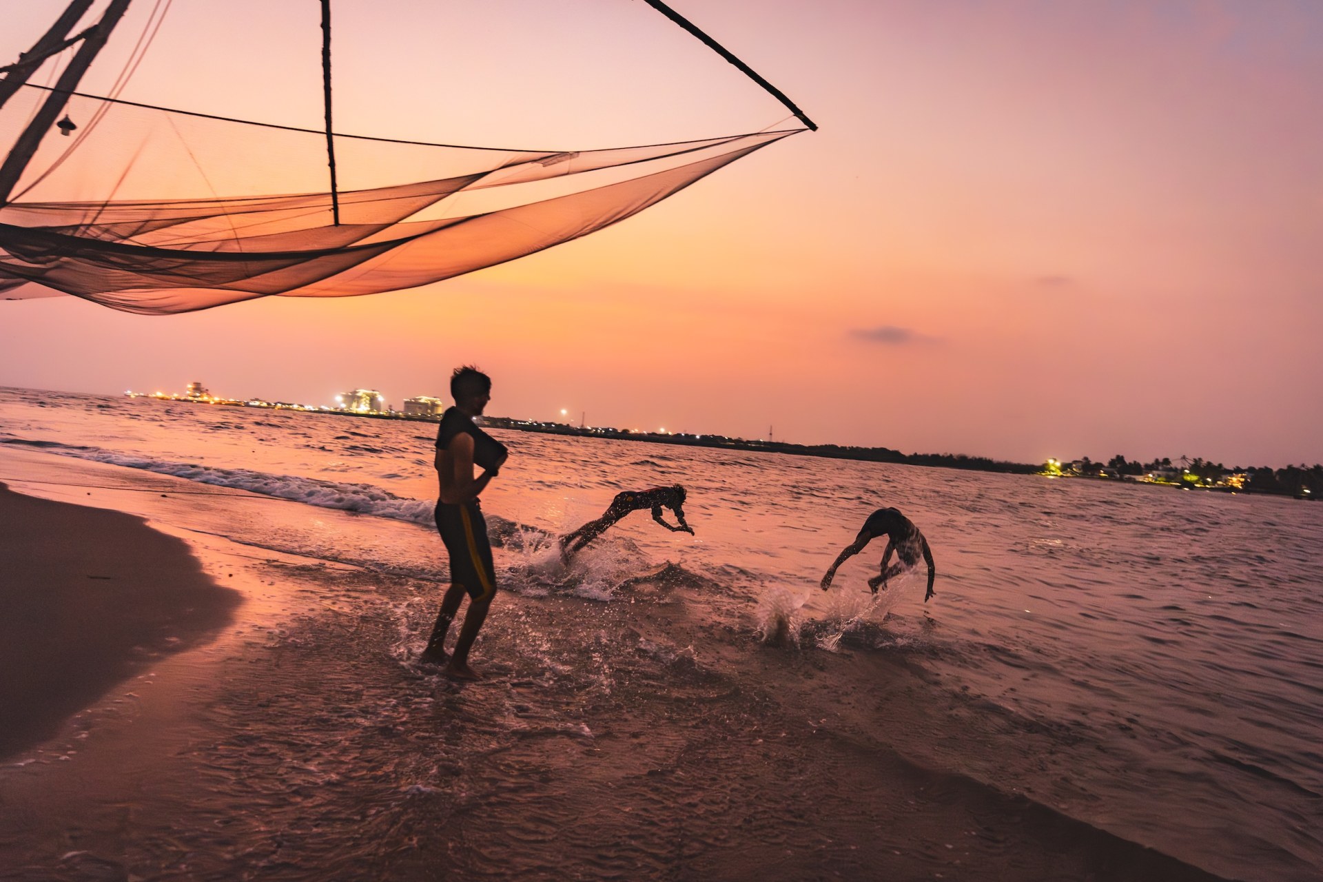 Boys doing flips into the sea beneath a Chinese fishing net at dusk in Kochi, India