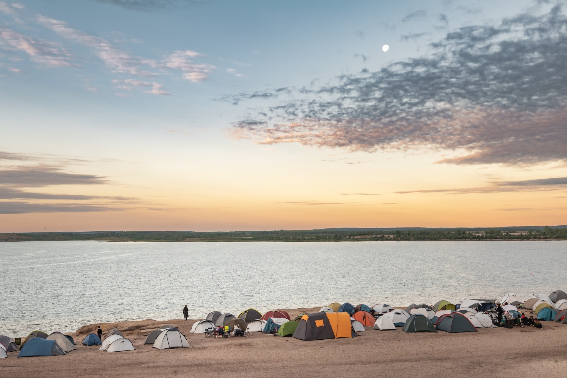 Tents on a sandy lakeshore beneath the evening sky and the moon at Feel Festival, Bergheider See, Brandenburg