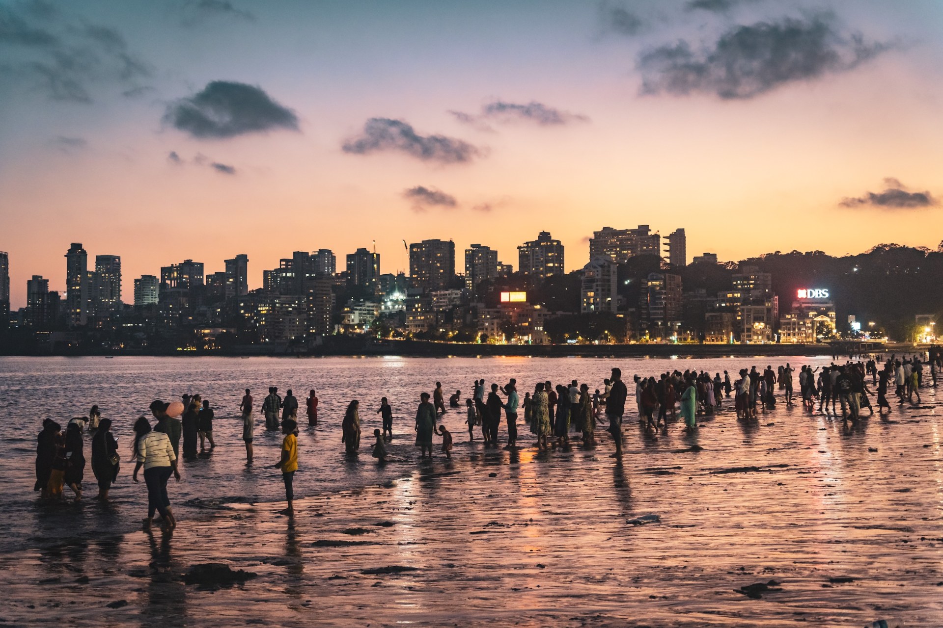 Crowds wading into the sea at dusk in front of the lit-up skyline of Mumbai, India