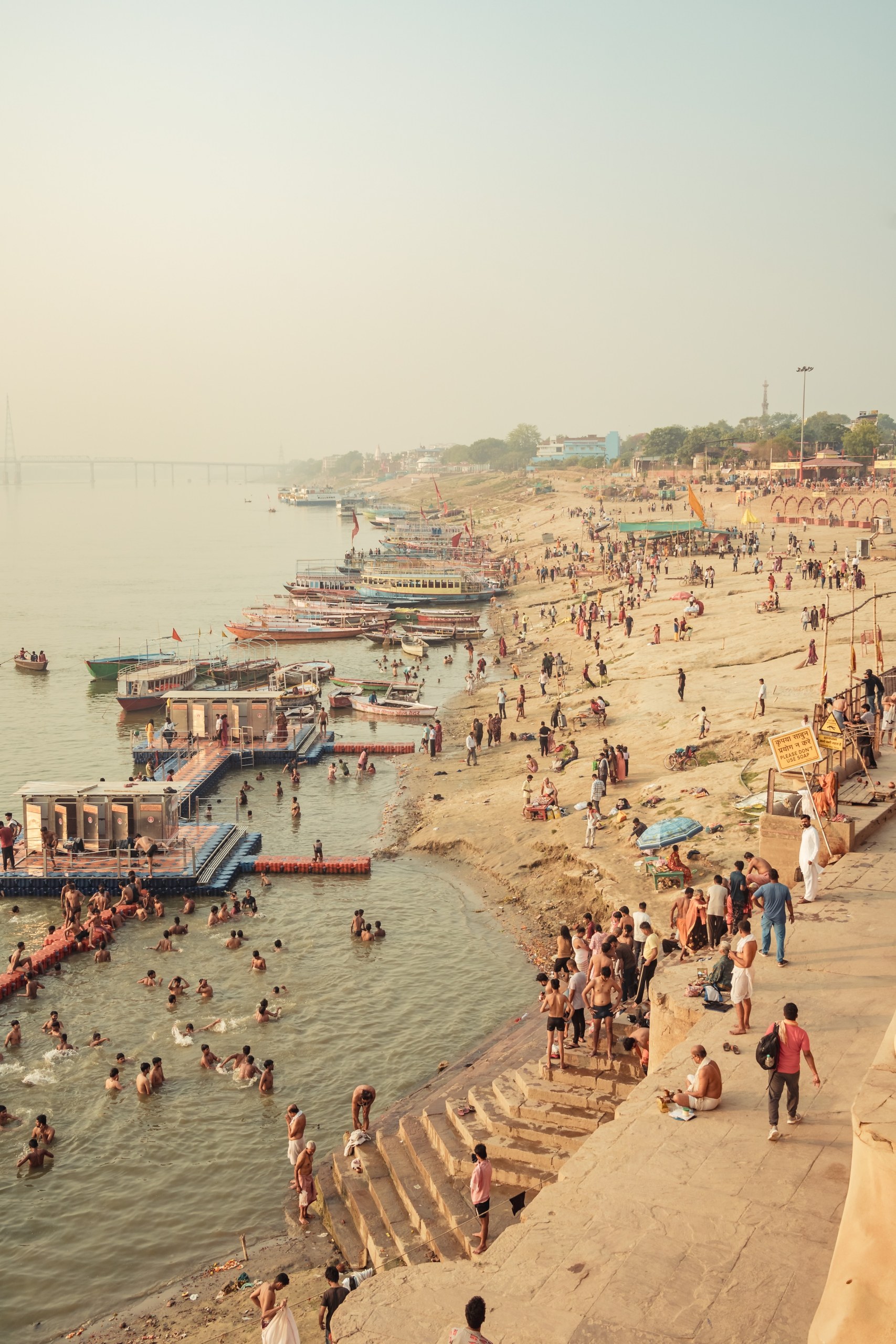 People bathing in the Ganges beside floating platforms and moored boats on a hazy morning, Varanasi, India